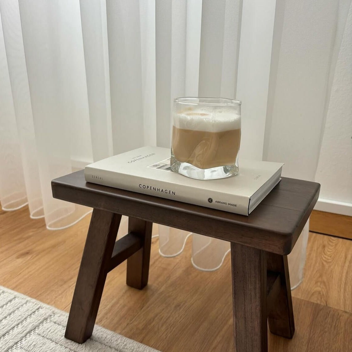 Diamond Twist Glas, präsentiert auf einem kleinen Holztisch mit einem Buch als Unterlage und köstlichem Cappuccino darin. Stilvolles Trinkglas mit markantem Design und ästhetischem Appeal. 